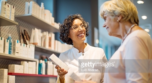 Mature female chemist explaining medication to senior customer in drugstore. Happy pharmacist showing medicine box and assisting senior woman.